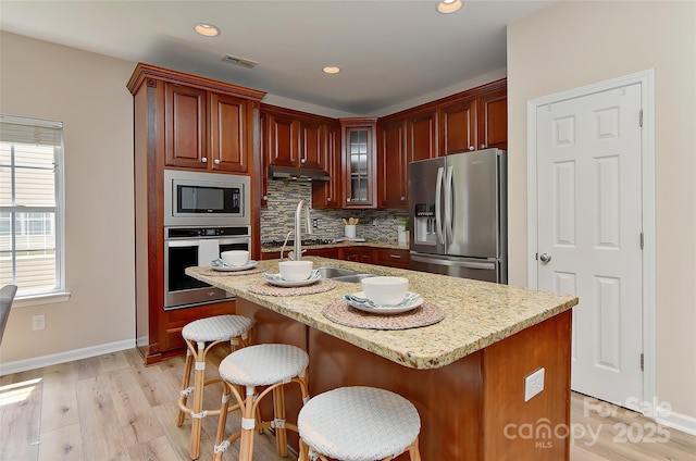 2017 Bridleside Dr, Indian Trail, NC 28079 - kitchen featuring stainless steel appliances, tasteful backsplash, light wood-type flooring, under cabinet range hood, and baseboards