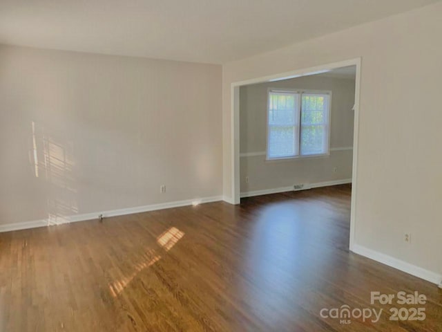 empty room featuring baseboards and dark wood finished floors