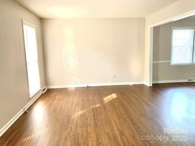 unfurnished room with dark wood-style flooring, visible vents, and baseboards