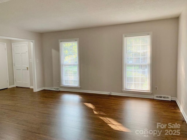 empty room with dark wood-style floors, visible vents, and baseboards