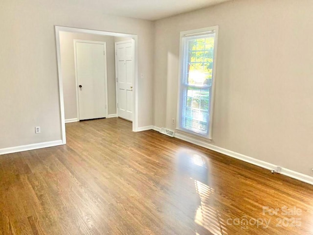 unfurnished room featuring wood finished floors, visible vents, and baseboards