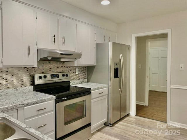 kitchen with light wood-style flooring, under cabinet range hood, stainless steel appliances, white cabinetry, and backsplash