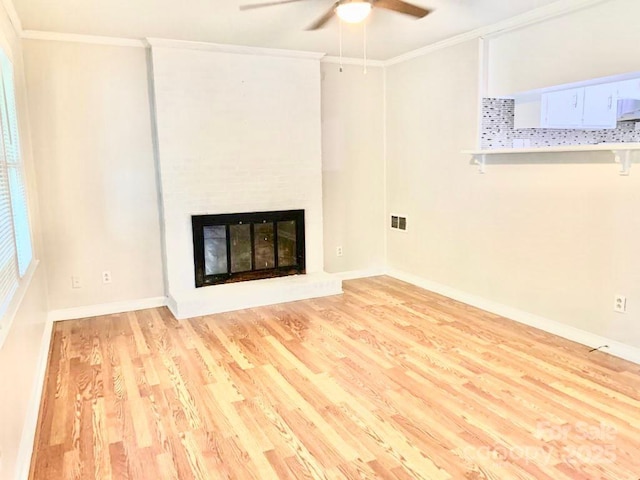 unfurnished living room with baseboards, visible vents, a glass covered fireplace, ornamental molding, and light wood-style floors