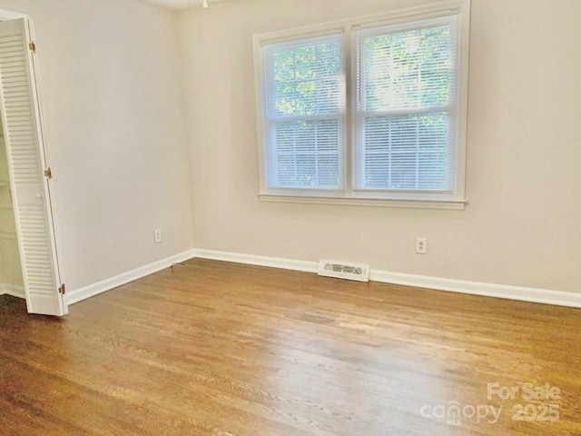 unfurnished room with baseboards, visible vents, and wood finished floors