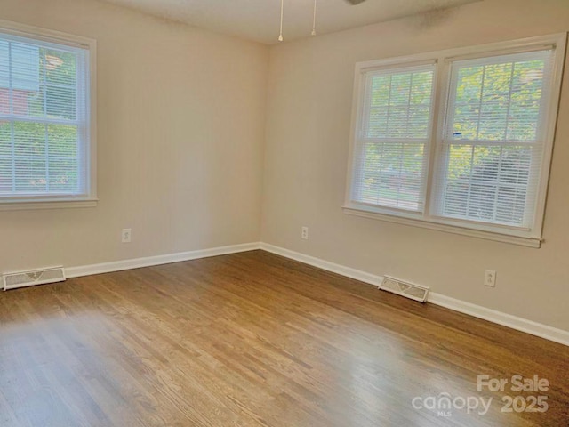 spare room with baseboards, visible vents, and wood finished floors