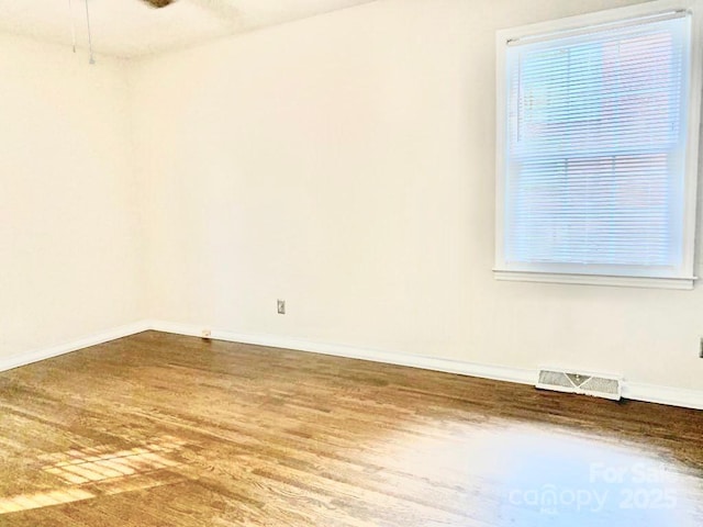 spare room with baseboards, visible vents, and wood finished floors