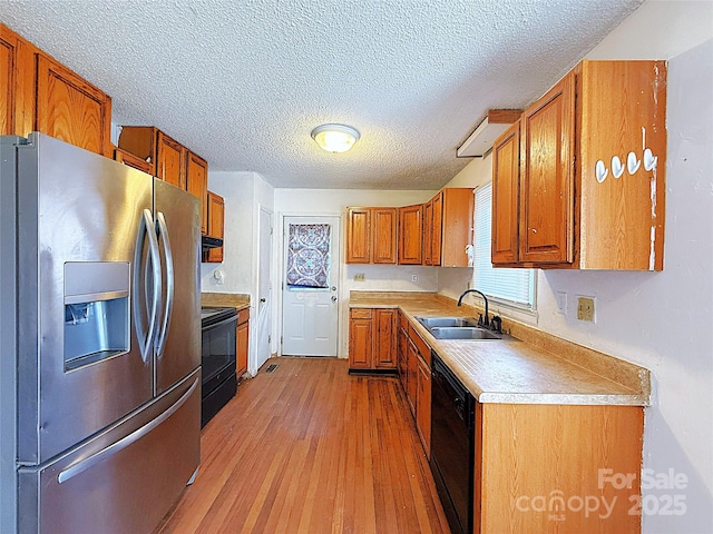 kitchen featuring light wood-style flooring, brown cabinets, light countertops, black appliances, and a sink