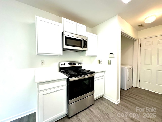 kitchen with appliances with stainless steel finishes, light countertops, washer / dryer, and white cabinetry