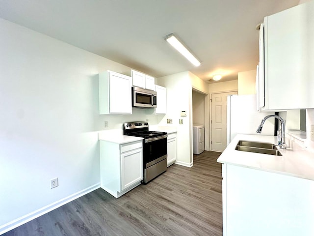 kitchen with wood finished floors, a sink, baseboards, appliances with stainless steel finishes, and washer / clothes dryer