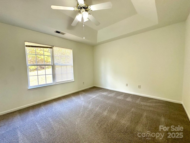 unfurnished room featuring ceiling fan, visible vents, baseboards, dark colored carpet, and a raised ceiling