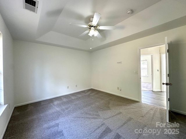 carpeted empty room featuring a ceiling fan, baseboards, visible vents, and a tray ceiling