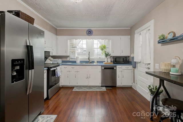 kitchen with a sink, under cabinet range hood, dark countertops, stainless steel appliances, and dark wood-style flooring