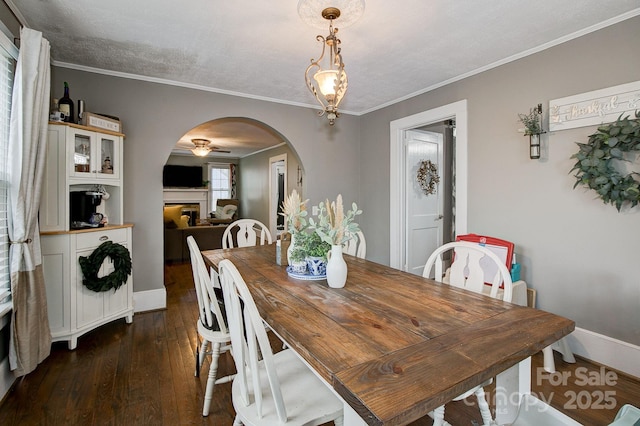 dining space with dark wood-style floors, baseboards, arched walkways, ceiling fan, and crown molding