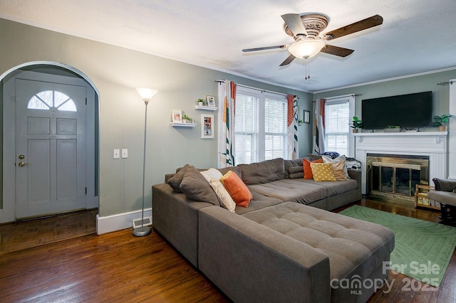 living area featuring a ceiling fan, a glass covered fireplace, wood finished floors, arched walkways, and crown molding