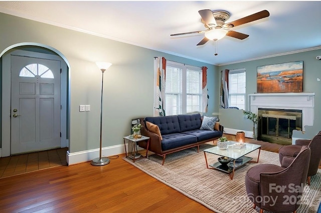 living area featuring wood finished floors, arched walkways, crown molding, baseboards, and ceiling fan