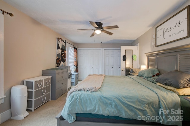 bedroom with a ceiling fan, multiple closets, and light carpet