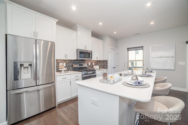 kitchen featuring stainless steel appliances, decorative backsplash, white cabinetry, a sink, and an island with sink