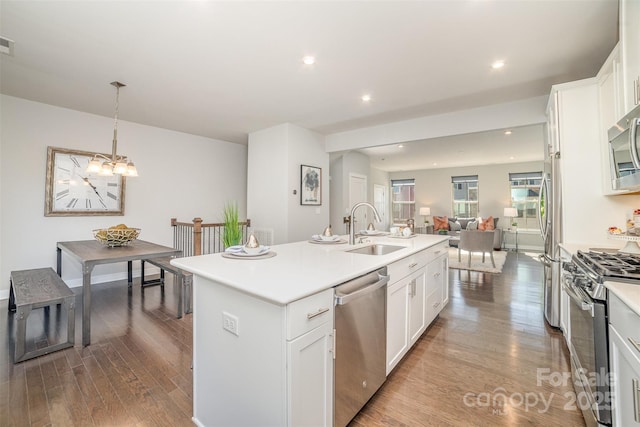 kitchen featuring an island with sink, appliances with stainless steel finishes, open floor plan, wood finished floors, and a sink