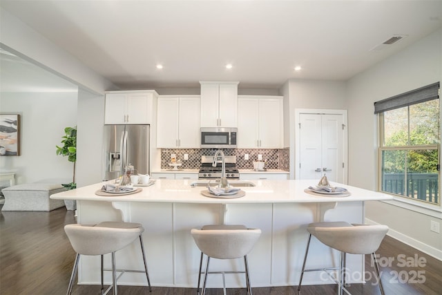 kitchen featuring stainless steel appliances, visible vents, decorative backsplash, white cabinets, and a large island with sink