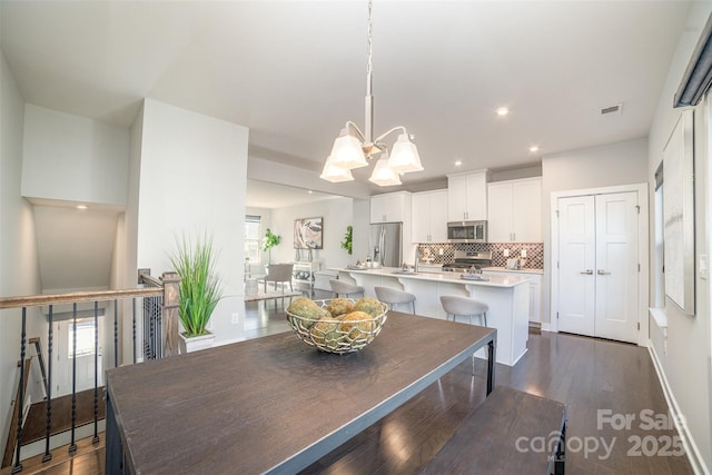 dining area with dark wood-style floors, recessed lighting, visible vents, and a notable chandelier