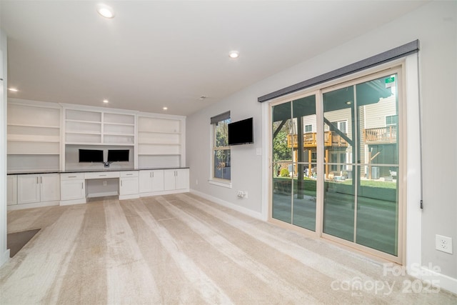 unfurnished living room with light carpet, recessed lighting, built in study area, and baseboards