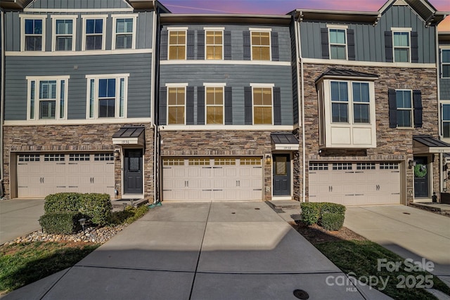 multi unit property with stone siding, an attached garage, board and batten siding, and driveway