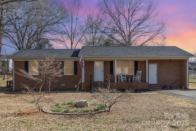 ranch-style house with covered porch, brick siding, crawl space, and roof with shingles