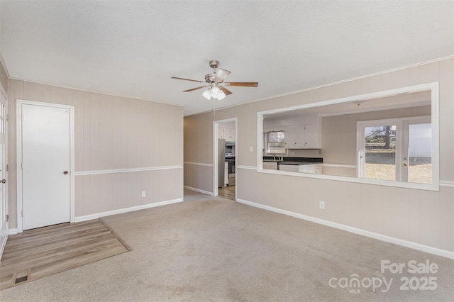 unfurnished living room with ornamental molding, carpet floors, ceiling fan, and a textured ceiling