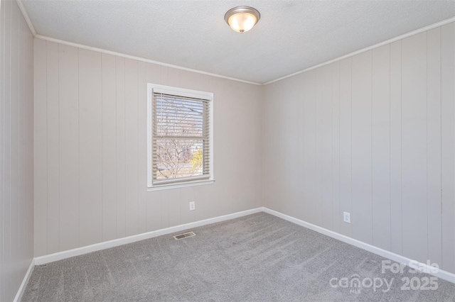 carpeted empty room with baseboards, a textured ceiling, visible vents, and crown molding