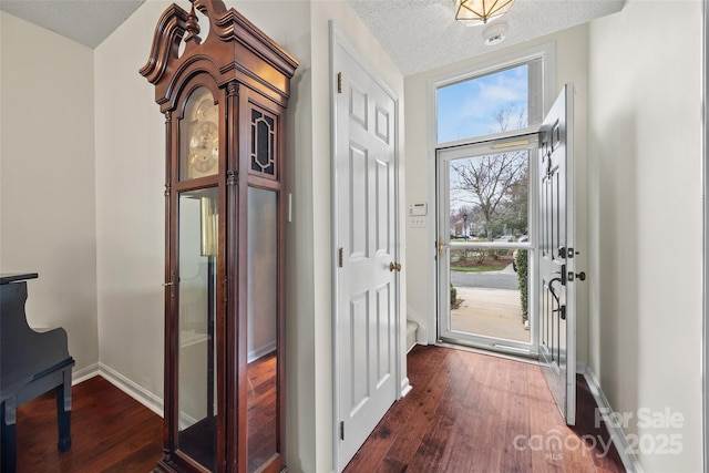 doorway to outside featuring dark wood-style floors, a textured ceiling, and baseboards