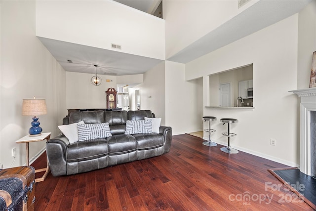 living room featuring a fireplace with raised hearth, a high ceiling, wood finished floors, visible vents, and baseboards