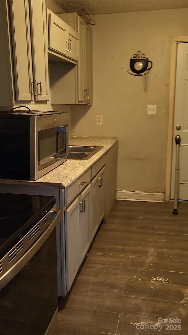 kitchen featuring electric range, dark wood finished floors, stainless steel microwave, light countertops, and a sink