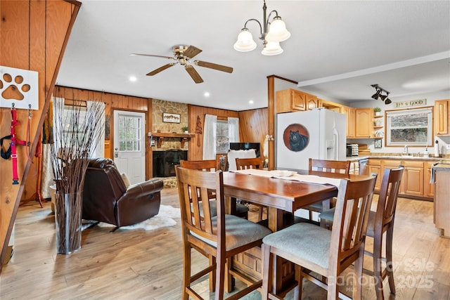 dining area with light wood-style floors, wooden walls, a fireplace, and ceiling fan