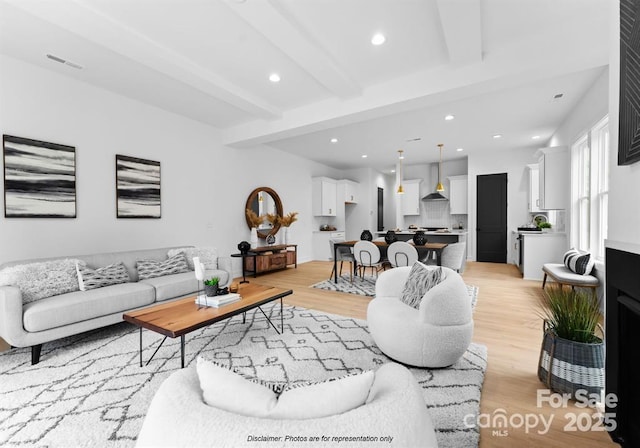 living area with light wood-style flooring, beamed ceiling, visible vents, and recessed lighting