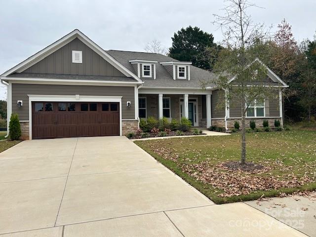 craftsman inspired home featuring an attached garage, board and batten siding, a front yard, stone siding, and driveway