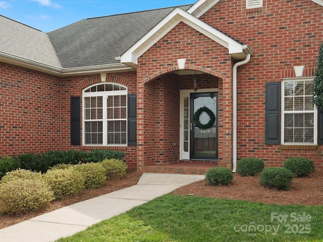 doorway to property with a shingled roof and brick siding