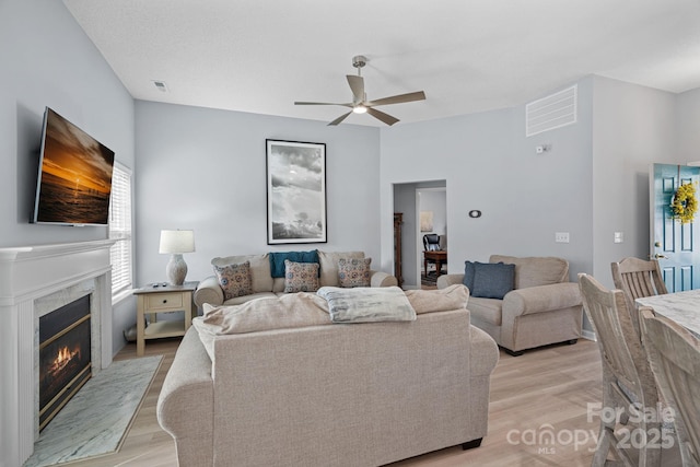 living room with ceiling fan, light wood finished floors, a premium fireplace, and visible vents