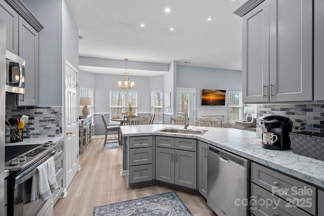 kitchen featuring stainless steel appliances, light wood finished floors, gray cabinetry, and a peninsula