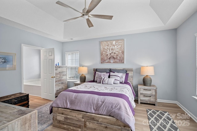 bedroom with ceiling fan, a tray ceiling, wood finished floors, and baseboards