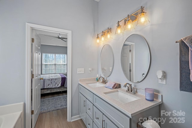 ensuite bathroom featuring double vanity, ceiling fan, a sink, and wood finished floors