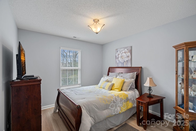 bedroom with baseboards, a textured ceiling, visible vents, and wood finished floors