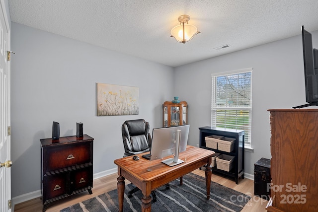 home office with light wood-type flooring, visible vents, a textured ceiling, and baseboards