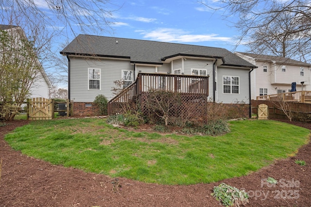 rear view of property featuring a deck, fence, roof with shingles, a lawn, and a gate