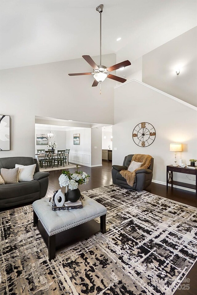 living area with baseboards, high vaulted ceiling, wood finished floors, and ceiling fan with notable chandelier