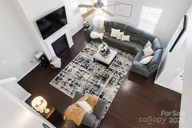living area featuring baseboards, a ceiling fan, wood finished floors, and a fireplace