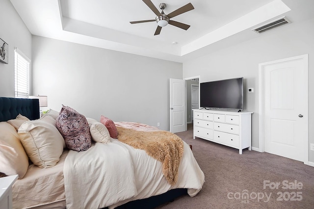 bedroom with dark carpet, a ceiling fan, baseboards, a tray ceiling, and visible vents