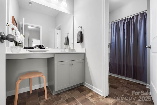 bathroom with vanity, stone finish floor, baseboards, curtained shower, and visible vents