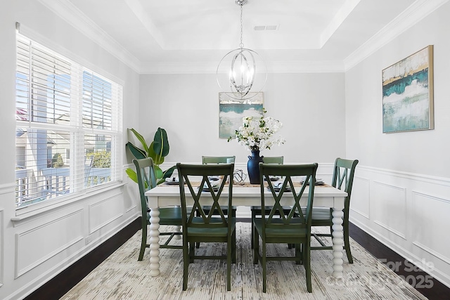 dining space featuring visible vents, wood finished floors, a raised ceiling, a chandelier, and a decorative wall