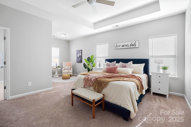 carpeted bedroom with a ceiling fan, baseboards, visible vents, and a raised ceiling