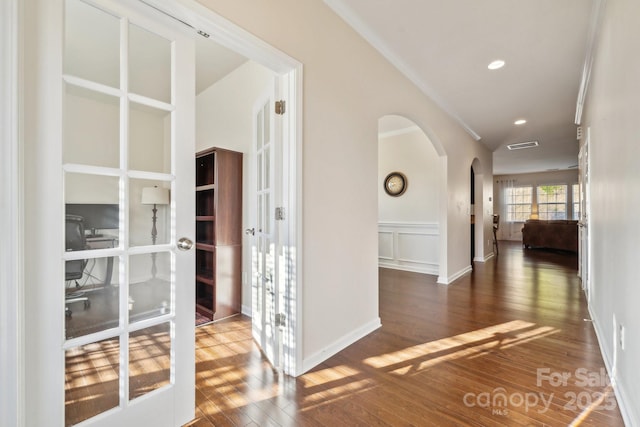 corridor with arched walkways, hardwood / wood-style flooring, recessed lighting, a decorative wall, and wainscoting